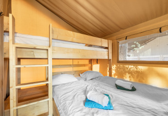 Vista interna di una tenda safari con letto a castello e letto matrimoniale, lenzuola bianche e asciugamani.