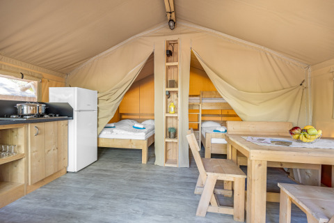 Vista interna di una tenda safari glamping con cucina, tavolo da pranzo e due aree notte separate.