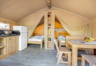 Vista interior de una tienda safari glamping con cocina, mesa de comedor y dos zonas de dormitorio separadas.