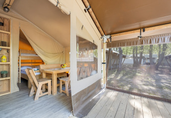 Interieur van een safaritent met houten meubilair, stapelbed en zicht op het bos door plastic wanden.