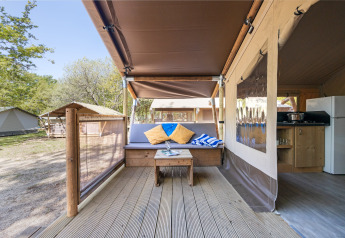 Gemütlicher Sitzbereich auf der Veranda eines Safarizeltes mit Sofa, Kissen, Tisch und Küche.