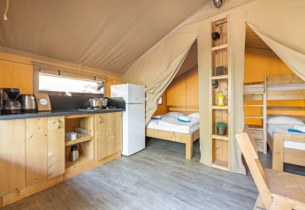 Interno di una tenda safari con angolo cottura, frigorifero, letto matrimoniale e letti a castello in legno.
