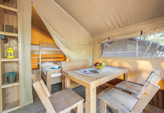 Intérieur d'une tente safari avec table à manger en bois, chaises, étagères et lits superposés visibles.