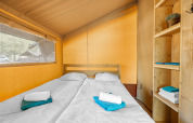 Interior of a safari tent with two single beds, wooden shelves, and neatly folded towels on each bed.
