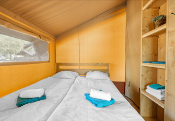 Interno di una tenda safari con due letti singoli, mensole in legno e asciugamani piegati su ogni letto.