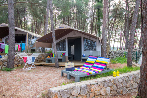 Tenda safari di lusso immersa nel bosco con sedie a sdraio colorate, terrazza e bucato steso.