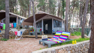 Tenda safari di lusso immersa nel bosco con sedie a sdraio colorate, terrazza e bucato steso.