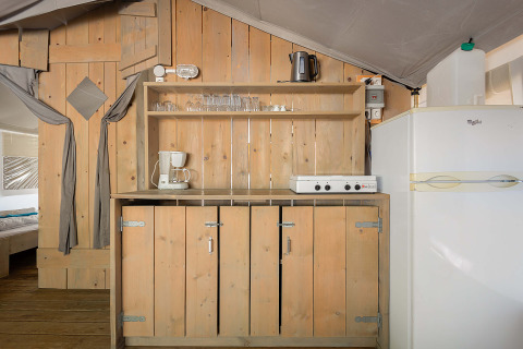 Area cucina nella Safari Tent Luxury al Camping Krk in Croazia, con credenze in legno e frigorifero.