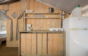 Coin cuisine de la Safari Tent Luxury au Camping Krk en Croatie, avec armoires en bois et réfrigérateur.