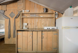 Zona de cocina en la Safari Tent Luxury de Camping Krk en Croacia, con muebles de madera y nevera blanca.