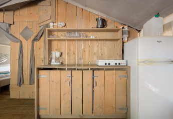 Area cucina nella Safari Tent Luxury al Camping Krk in Croazia, con credenze in legno e frigorifero.
