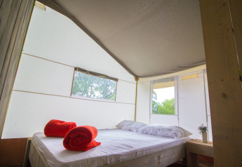 Vista interna della Safari Tent Luxury con letto matrimoniale e asciugamani rossi al Camping Krk, Croazia.