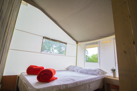 Vista interna della Safari Tent Luxury con letto matrimoniale e asciugamani rossi al Camping Krk, Croazia.