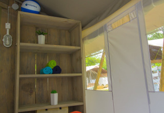 Interior de una tienda safari de lujo en Camping Krk, Croacia, con estantería, toallas y cama blanca.