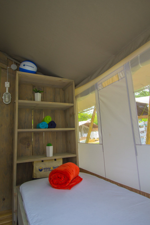 Interno di una tenda safari di lusso al Camping Krk in Croazia, con mensola, letto e asciugamani colorati.