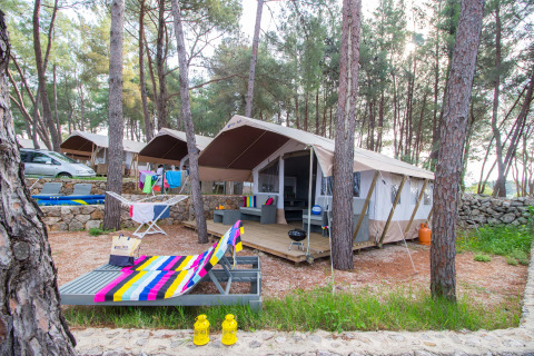 Tenda safari di lusso al Camping Krk in Croazia tra i pini, sdraio colorata e terrazza arredata.
