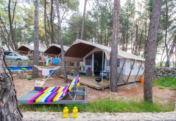 Luxury safari tent at Camping Krk in Croatia with lounge, vibrant towels, and surrounded by pine trees.