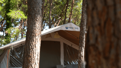 Safari Tent Luxury al Camping Krk in Croazia, circondata da alti alberi, vista dall'esterno di giorno.