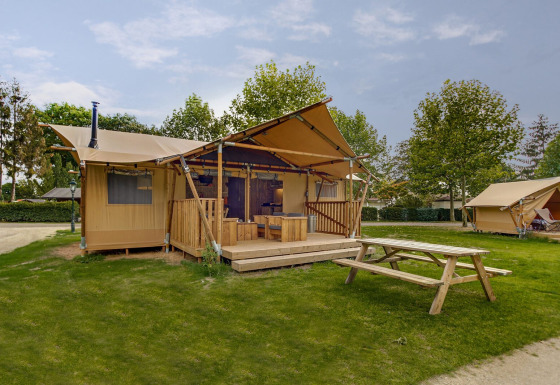 Alojamiento glamping con tienda de campaña de lujo, terraza de madera y banco en un entorno verde.