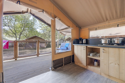 Intérieur de la Safari tent Cozy avec cuisine ouverte, terrasse et vue sur d'autres tentes en plein air.