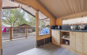 Innenansicht des Safari-Zeltes Cozy mit Küchenbereich, Terrasse und Blick auf andere Zelte im Grünen.
