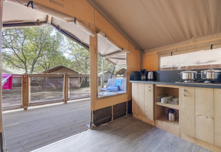 Innenansicht des Safari-Zeltes Cozy mit Küchenbereich, Terrasse und Blick auf andere Zelte im Grünen.