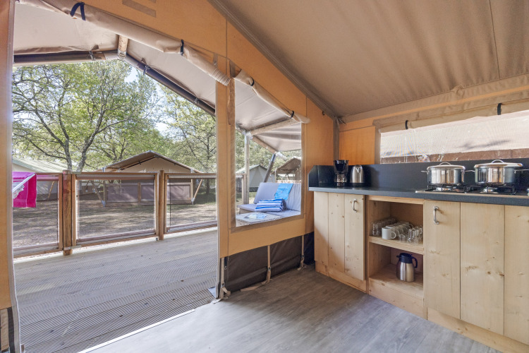 Interior of Safari tent Cozy featuring an open kitchen, terrace view, and nearby tents among the trees.