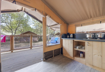 Intérieur de la Safari tent Cozy avec cuisine ouverte, terrasse et vue sur d'autres tentes en plein air.