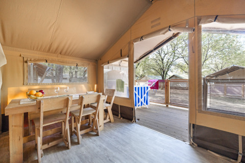 Vista interior de la tienda Safari tent Cozy con mesa de madera, sillas y terraza con vistas a otras tiendas.