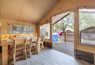 Binnenaanzicht van Safari tent Cozy met houten tafel, stoelen en zicht op terras en andere safaritenten.