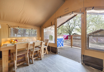 Vista interior de la tienda Safari tent Cozy con mesa de madera, sillas y terraza con vistas a otras tiendas.