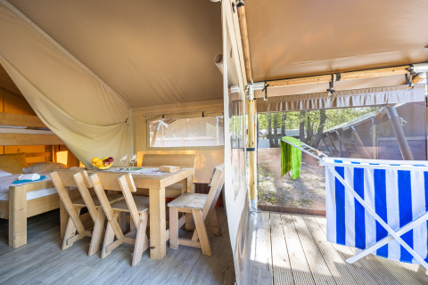 Interno della tenda Safari Cozy con mobili in legno, letti a castello e terrazza con stendino.