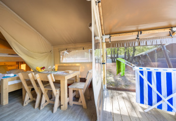 Interno della tenda Safari Cozy con mobili in legno, letti a castello e terrazza con stendino.