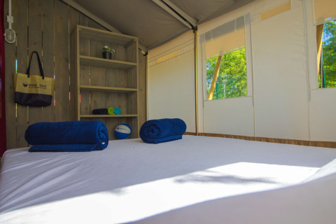 Interior de una tienda safari con cama, toallas azules y estantería en Camping Polari en Croacia.