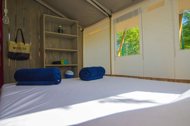 Interior of a safari tent with bed, blue towels, shelves and windows at Camping Polari in Croatia.