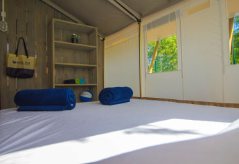 Interior de una tienda safari con cama, toallas azules y estantería en Camping Polari en Croacia.