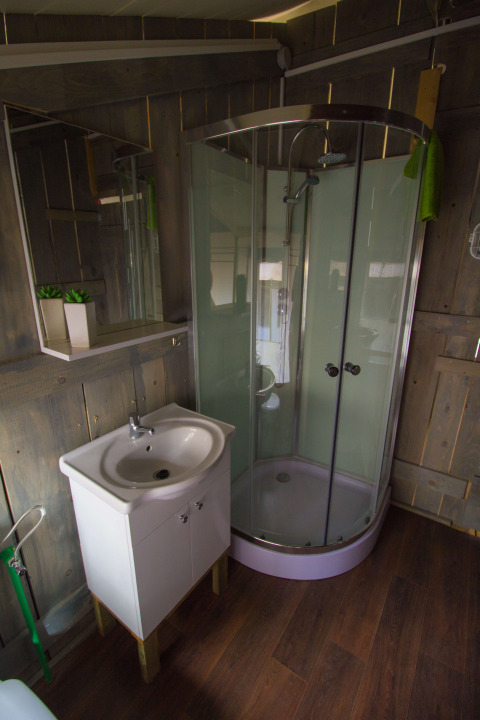 Baño con cabina de ducha, lavabo y paredes de madera en una tienda safari en Camping Polari, Croacia.