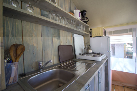 Keuken in een safaritent op Camping Polari in Kroatië met gootsteen, kookplaat, koelkast en planken.