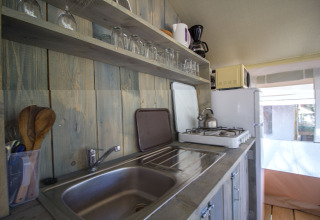 Safari tent kitchen at Camping Polari in Croatia, featuring a sink, stove, fridge, shelves and utensils.