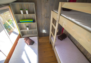 Vista interior de una tienda safari con literas, estantería y luz natural en Camping Polari, Croacia.