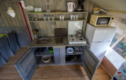 Compact safari tent kitchen at Camping Polari, Croatia, with fridge, microwave, stove, and utensils.