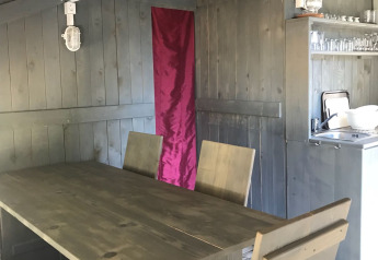 Indendørs spiseområde i et safaritelt med træmøbler, aircondition og lille køkken ved Camping Polari.