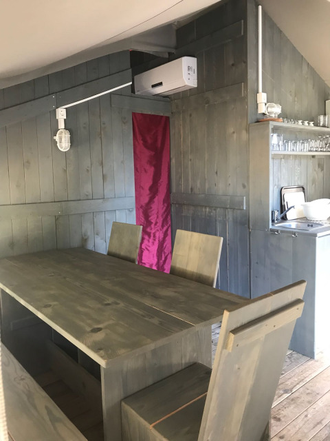 Indendørs spiseområde i et safaritelt med træmøbler, aircondition og lille køkken ved Camping Polari.