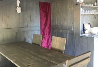 Indendørs spiseområde i et safaritelt med træmøbler, aircondition og lille køkken ved Camping Polari.