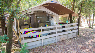 Tenda safari con veranda, coperte colorate, cucina, aria condizionata e ambiente boschivo privato.