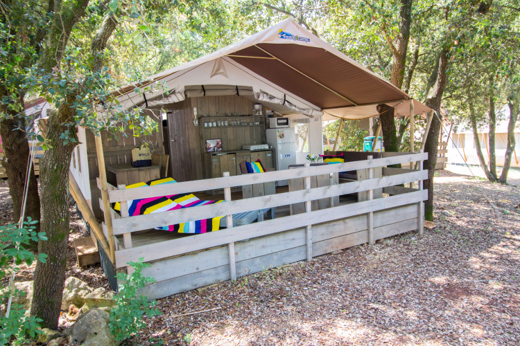 Safari tent with porch, colorful blankets, kitchen facilities, air conditioning and wooded setting.