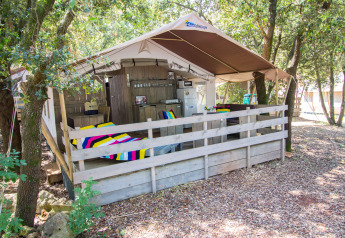 Tenda safari con veranda, coperte colorate, cucina, aria condizionata e ambiente boschivo privato.