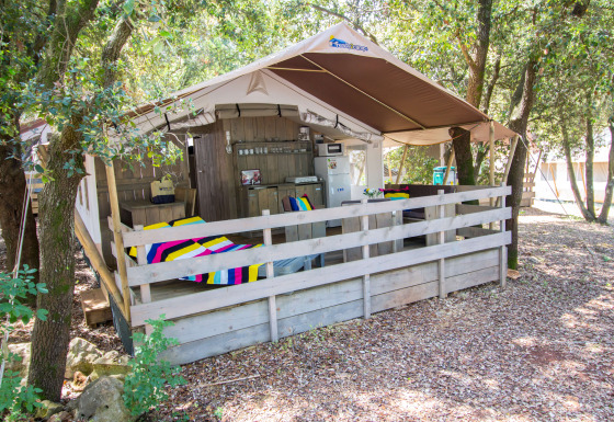 Tenda safari con veranda, coperte colorate, cucina, aria condizionata e ambiente boschivo privato.