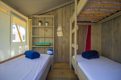Vista interior de tienda safari con literas, estantería y ventana en Camping Polari en Croacia.
