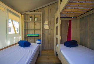 Vista interior de tienda safari con literas, estantería y ventana en Camping Polari en Croacia.